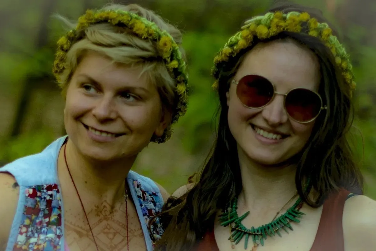 Two women wearing flower wreaths smiling outdoors